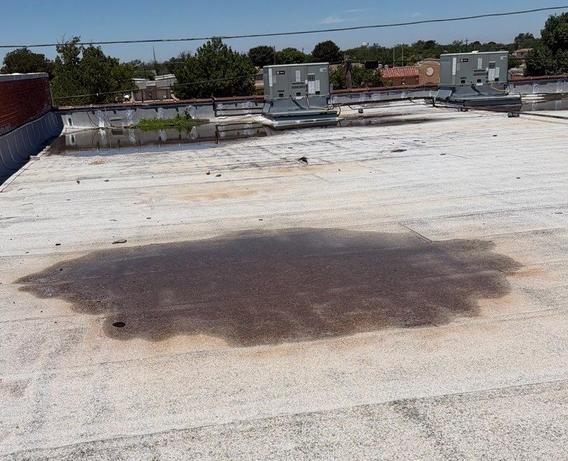 Standing water and dark ponding stains on a flat commercial roof membrane